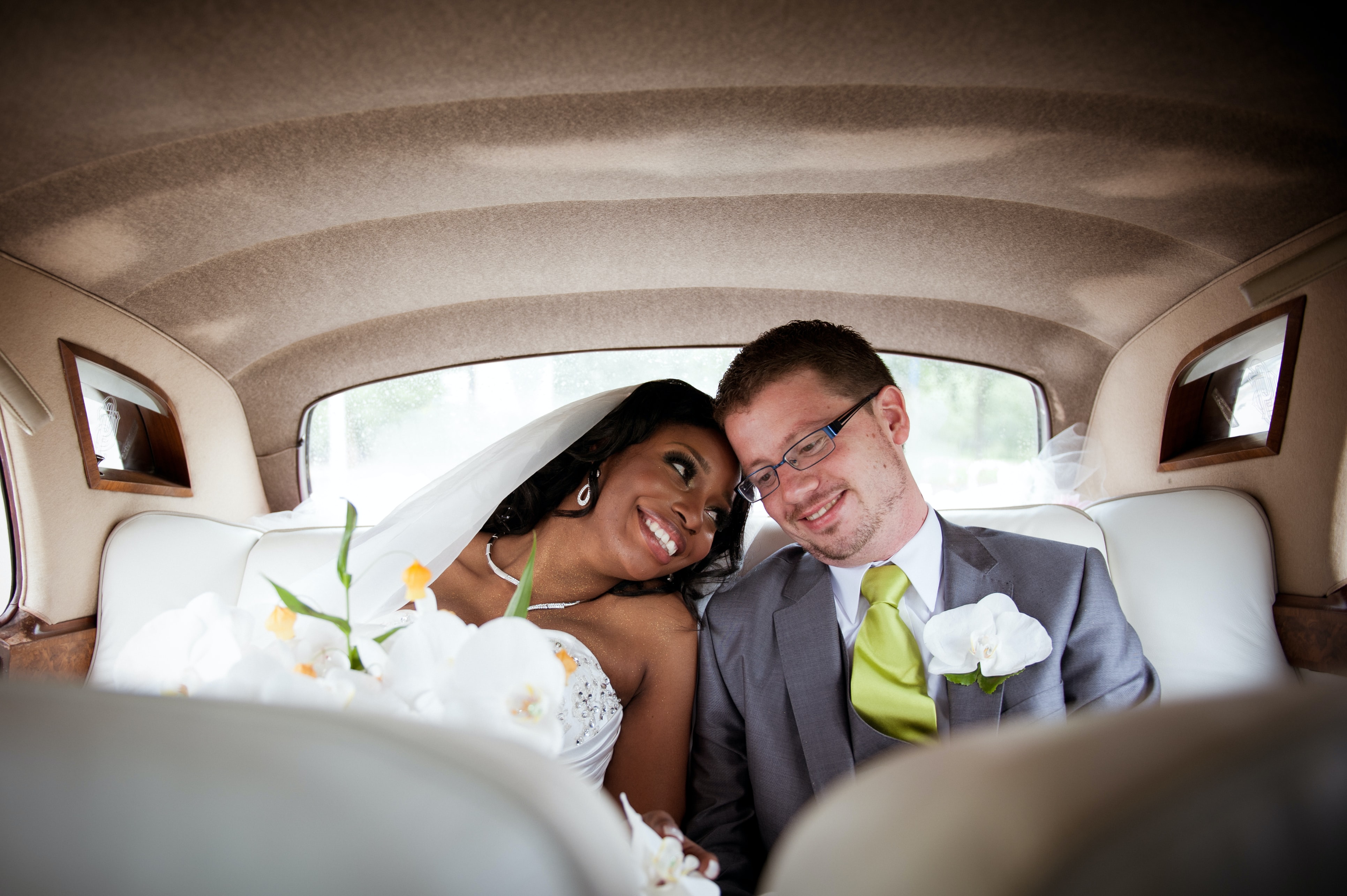Deux mariés dans une voiture. Une fillle et un garçon en tenues de mariage se souriant entre eux.